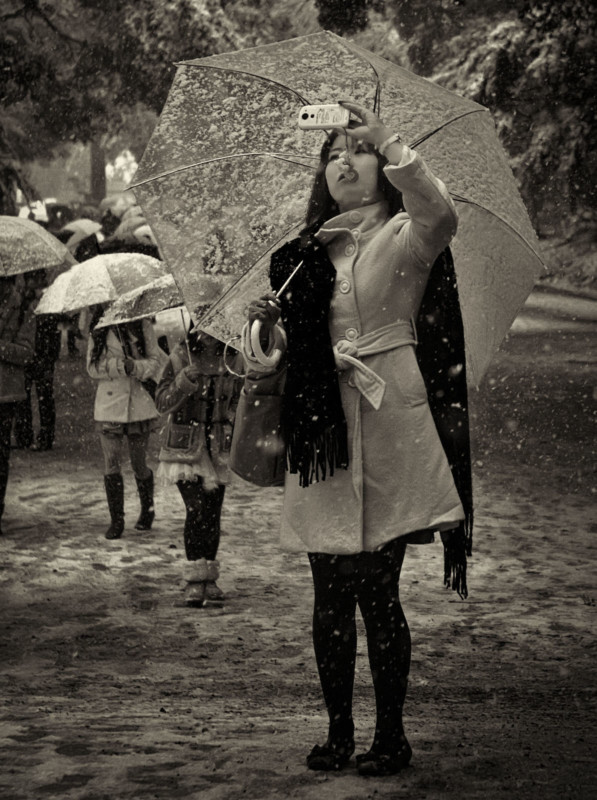 A woman holding an umbrella in snowfall while shooting a photo