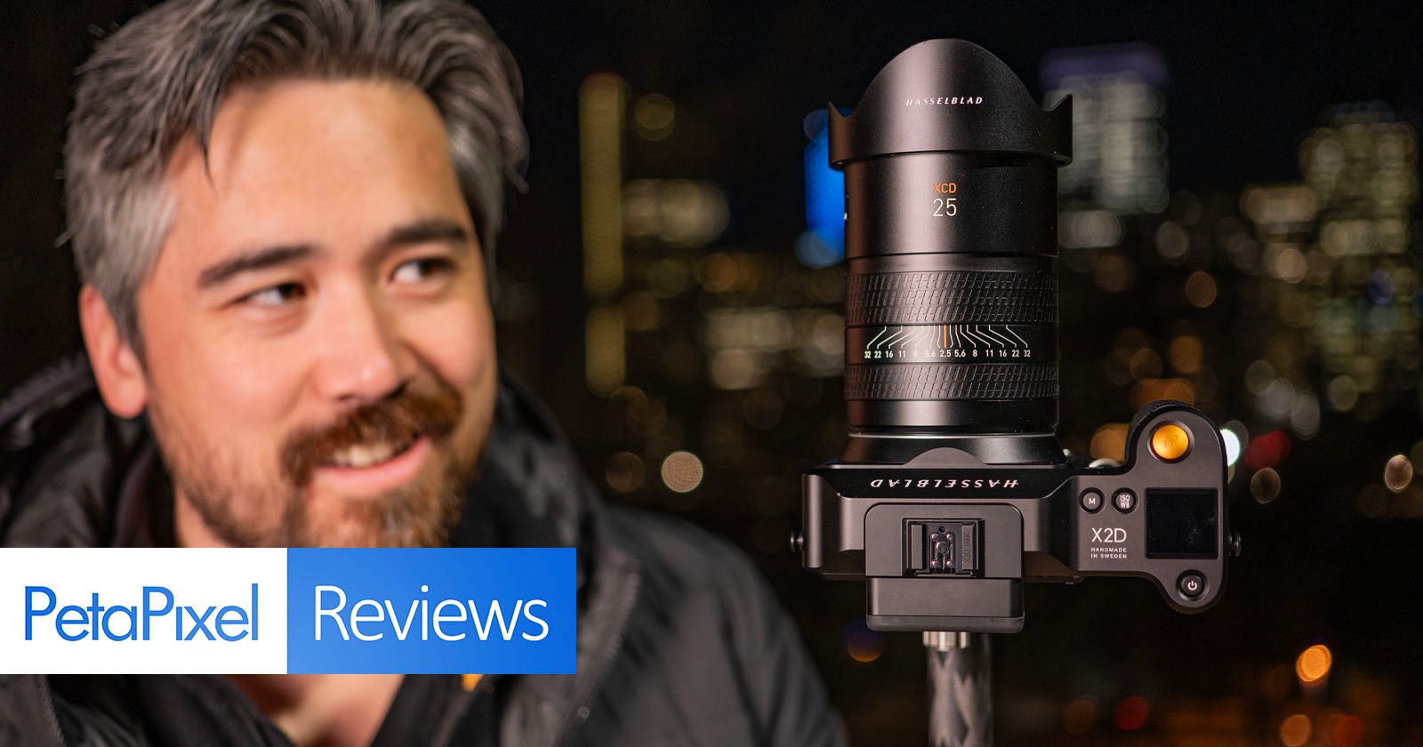A man with a slight smile looks at a camera mounted on a tripod in the foreground, with a city's blurry lights in the background. the image includes a petapixel reviews label.